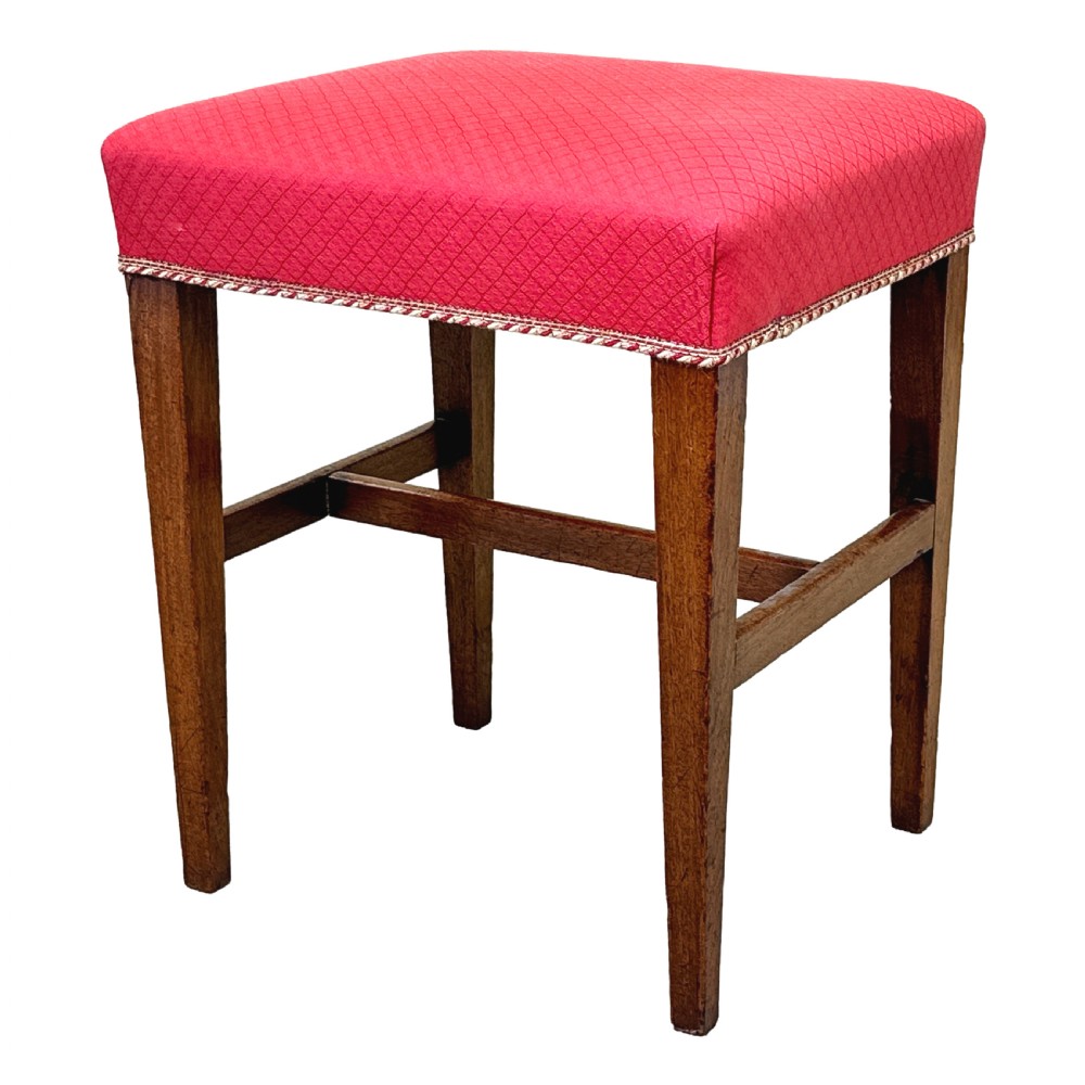 An 18th-century Georgian mahogany stool featuring a square red patterned upholstered top with braided trim, supported by four tapered wood legs and an H-stretcher.