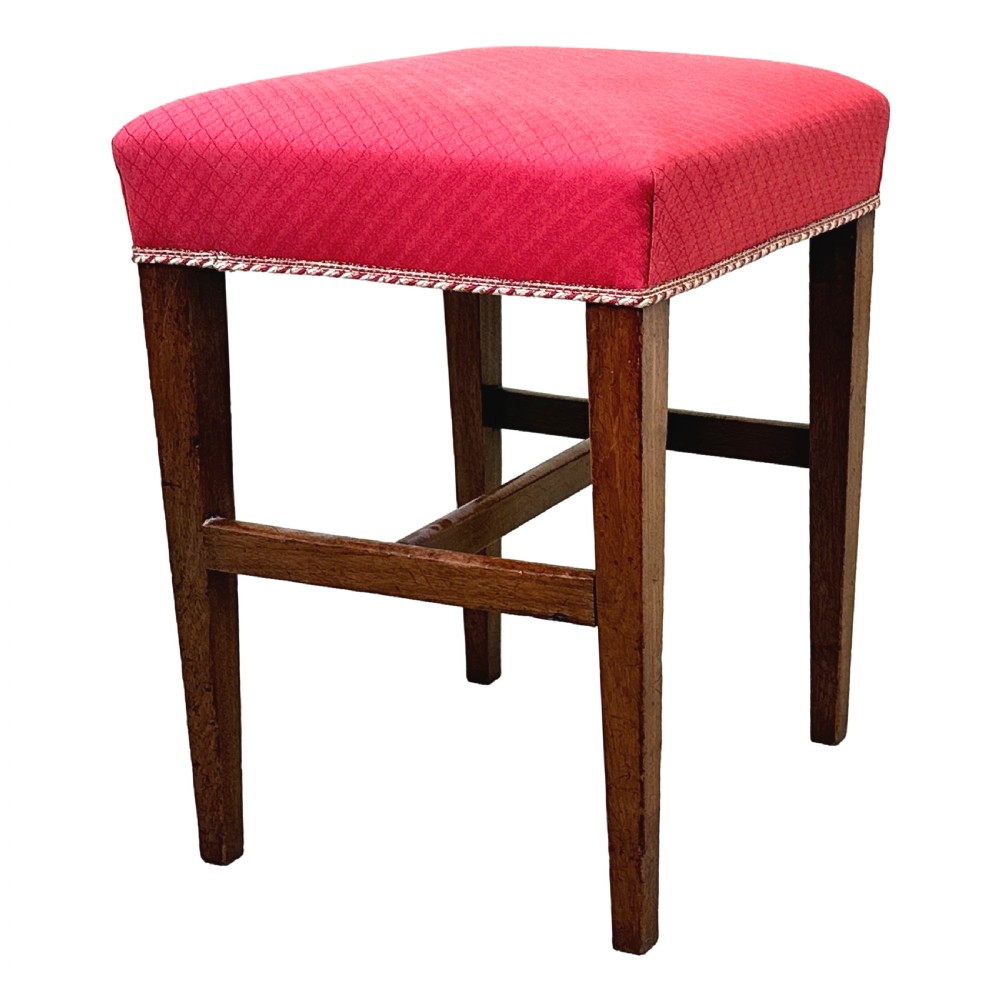 An 18th-century Georgian mahogany stool featuring a square red patterned upholstered top with braided trim, supported by four tapered wood legs and an H-stretcher. View V