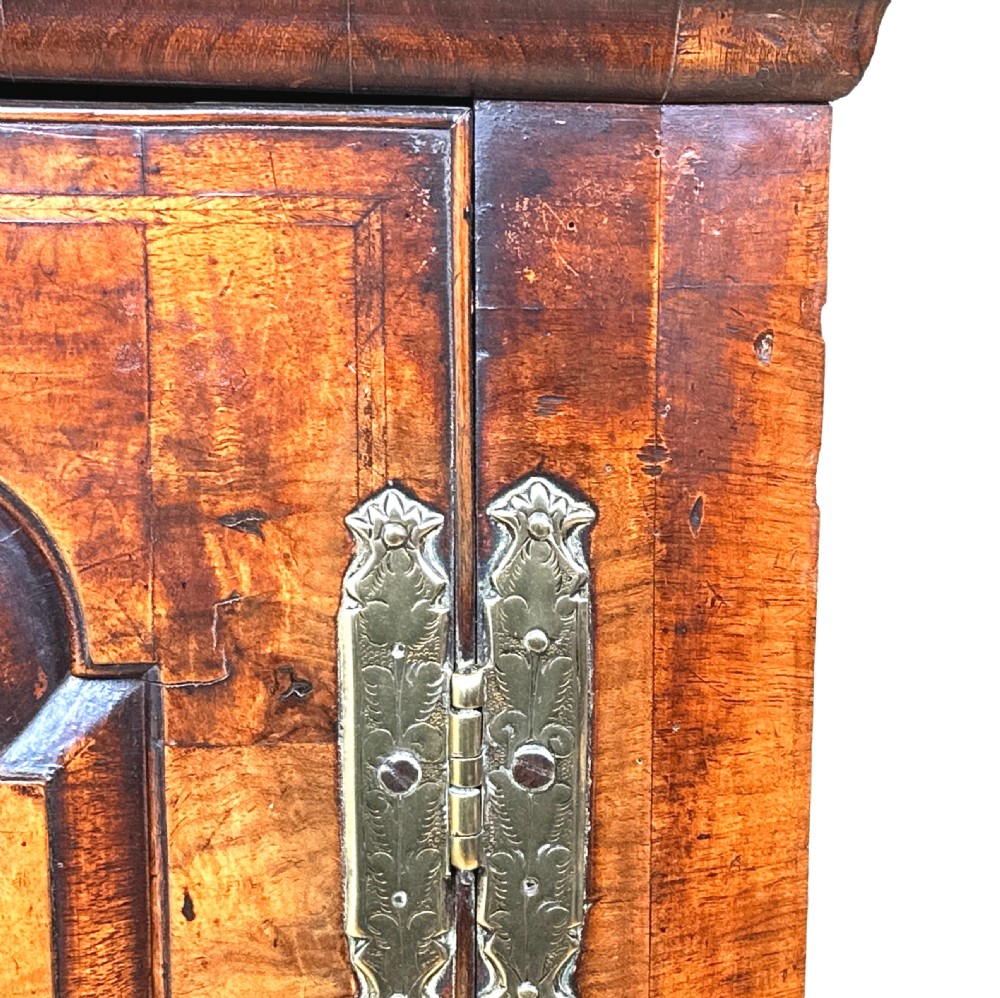 An early 18th-century walnut corner cupboard featuring a raised arched door panel, engraved brass H-hinges, and a moulded cornice. View II
