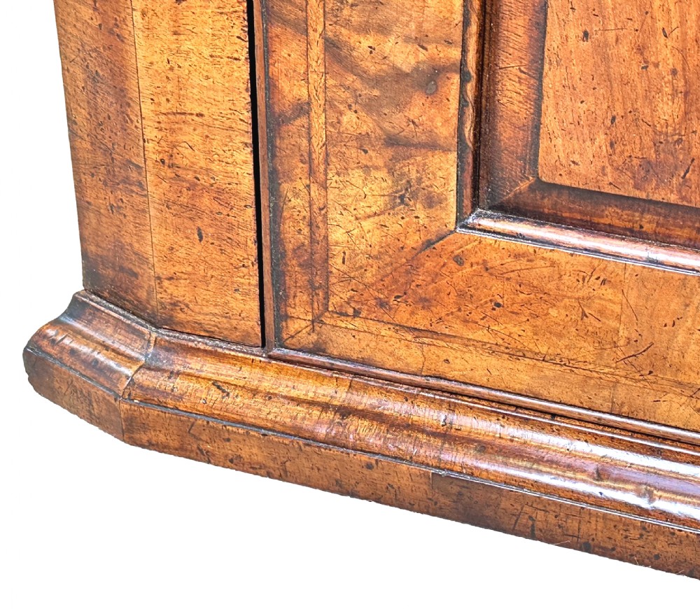 An early 18th-century walnut corner cupboard featuring a raised arched door panel, engraved brass H-hinges, and a moulded cornice. View V