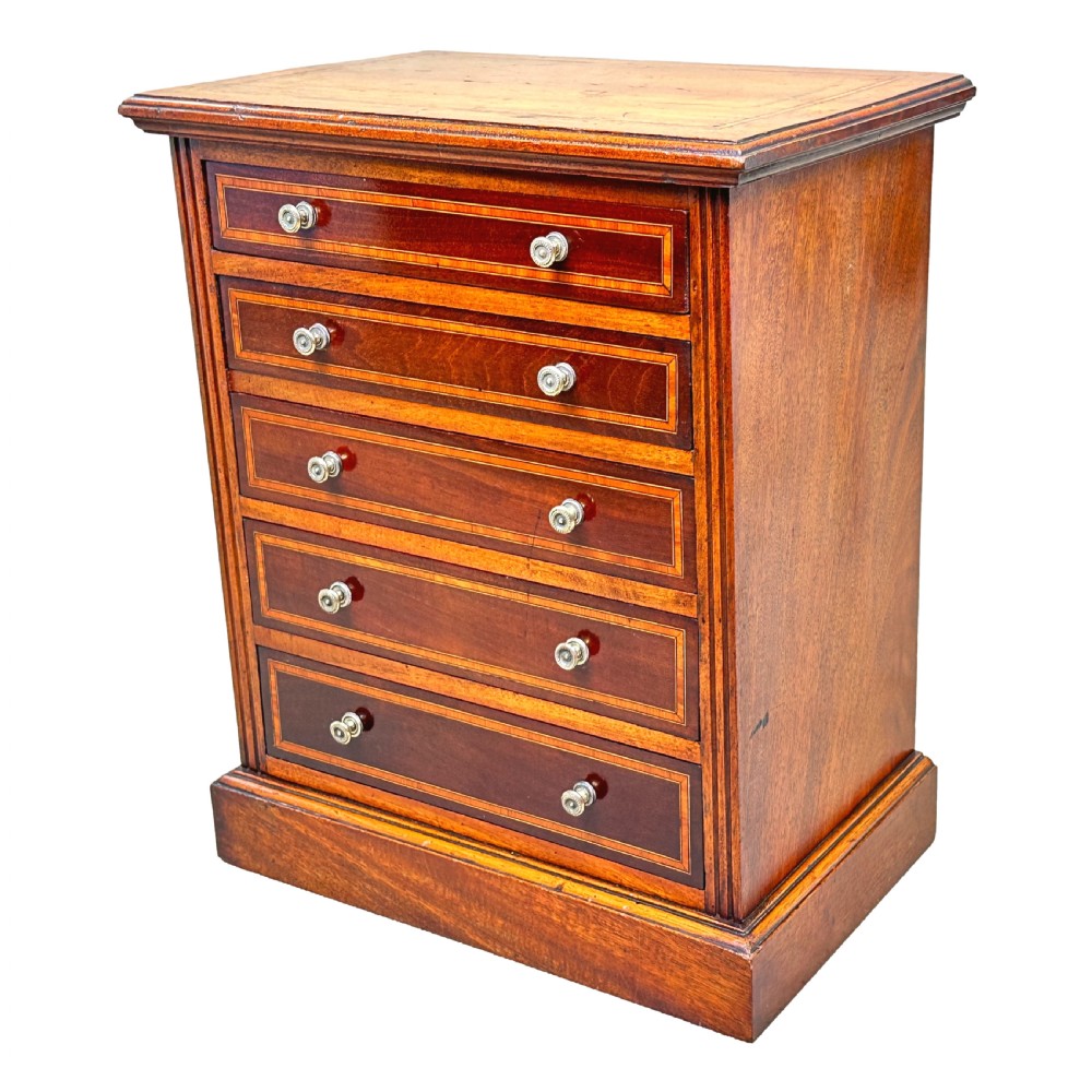 A 19th-century walnut miniature chest of five graduated drawers featuring inlaid crossbanded borders and turned handles on a solid plinth base.