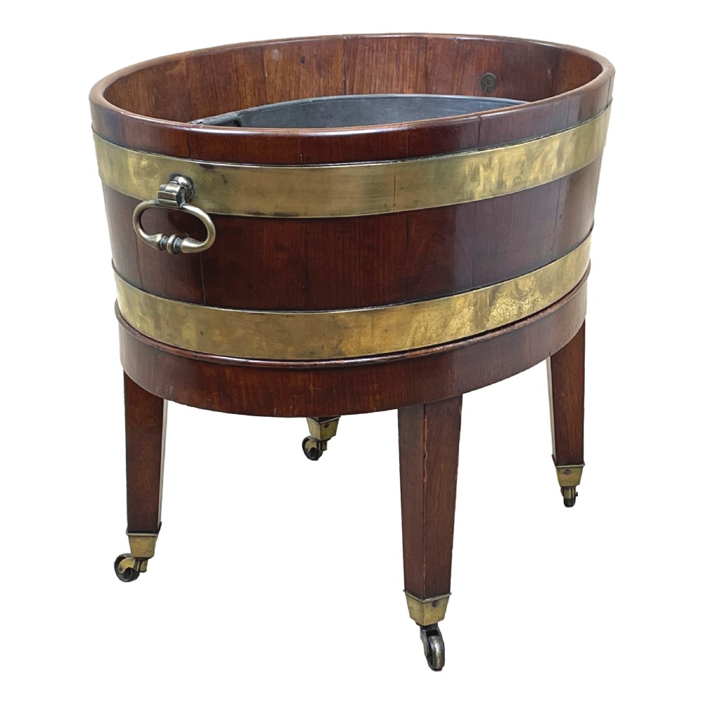 An oval coopered mahogany wine cooler featuring two brass binding hoops, carrying handles, and four tapered legs with brass castors. View III