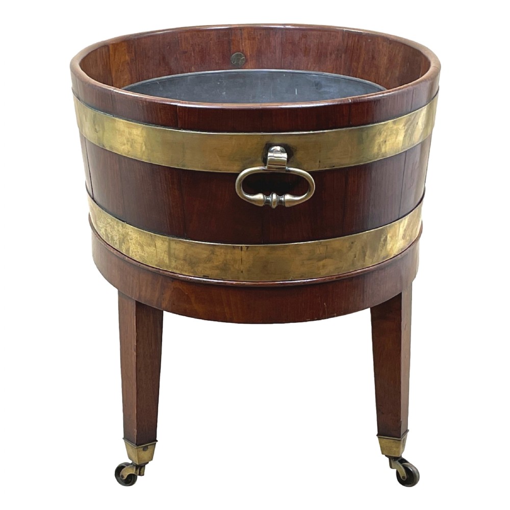 An oval coopered mahogany wine cooler featuring two brass binding hoops, carrying handles, and four tapered legs with brass castors. View VII