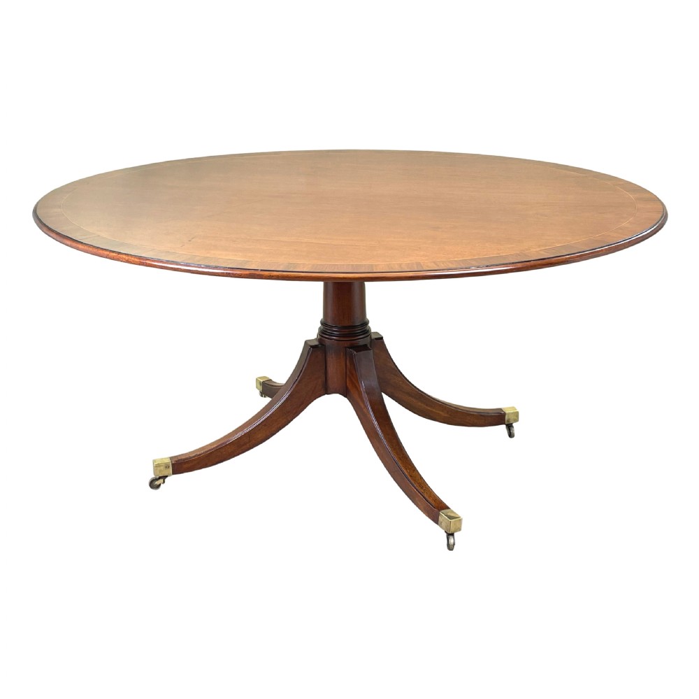 An 18th-century Georgian oval mahogany breakfast table with crossbanded inlay, set on a central turned pedestal with four splayed legs and brass castors.