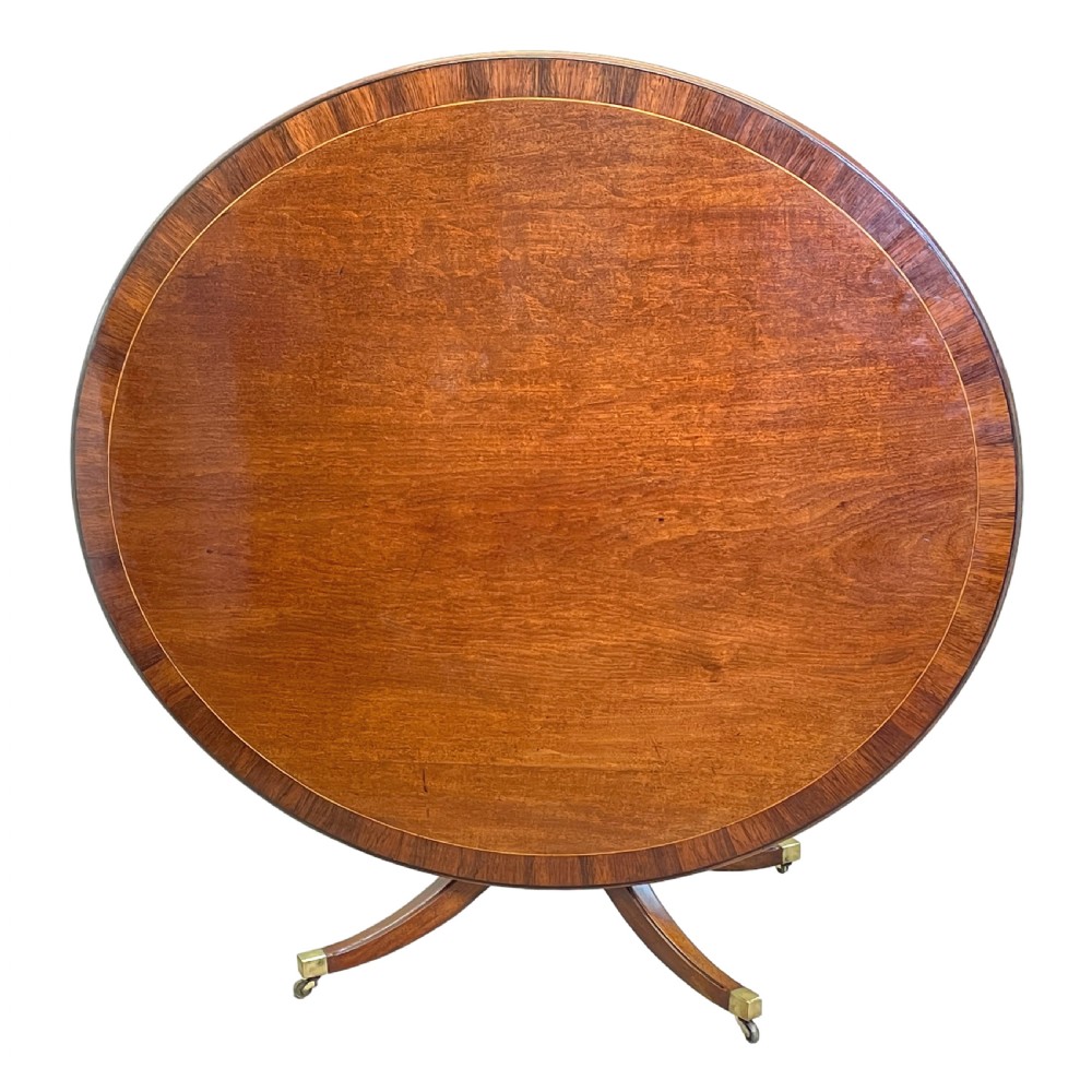 An 18th-century Georgian oval mahogany breakfast table with crossbanded inlay, set on a central turned pedestal with four splayed legs and brass castors. View III