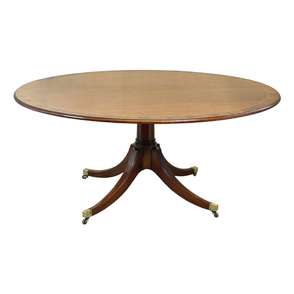An 18th-century Georgian oval mahogany breakfast table with crossbanded inlay, set on a central turned pedestal with four splayed legs and brass castors. View IV