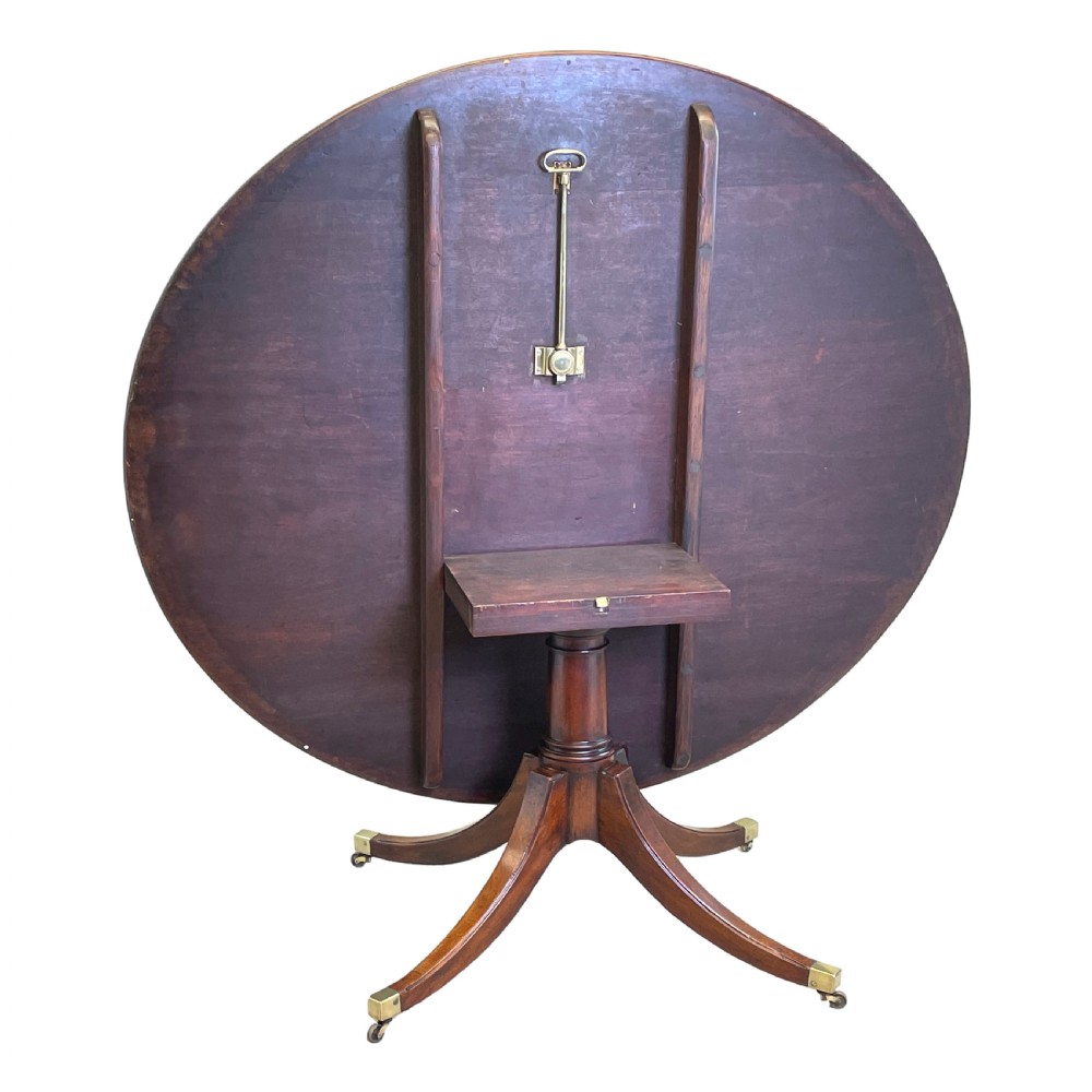 An 18th-century Georgian oval mahogany breakfast table with crossbanded inlay, set on a central turned pedestal with four splayed legs and brass castors. View V