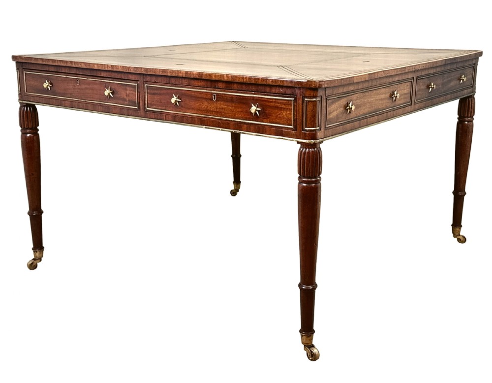 A square Regency mahogany partners writing table with a leather insert top, brass star handles on twin drawers, and fluted legs on castors.