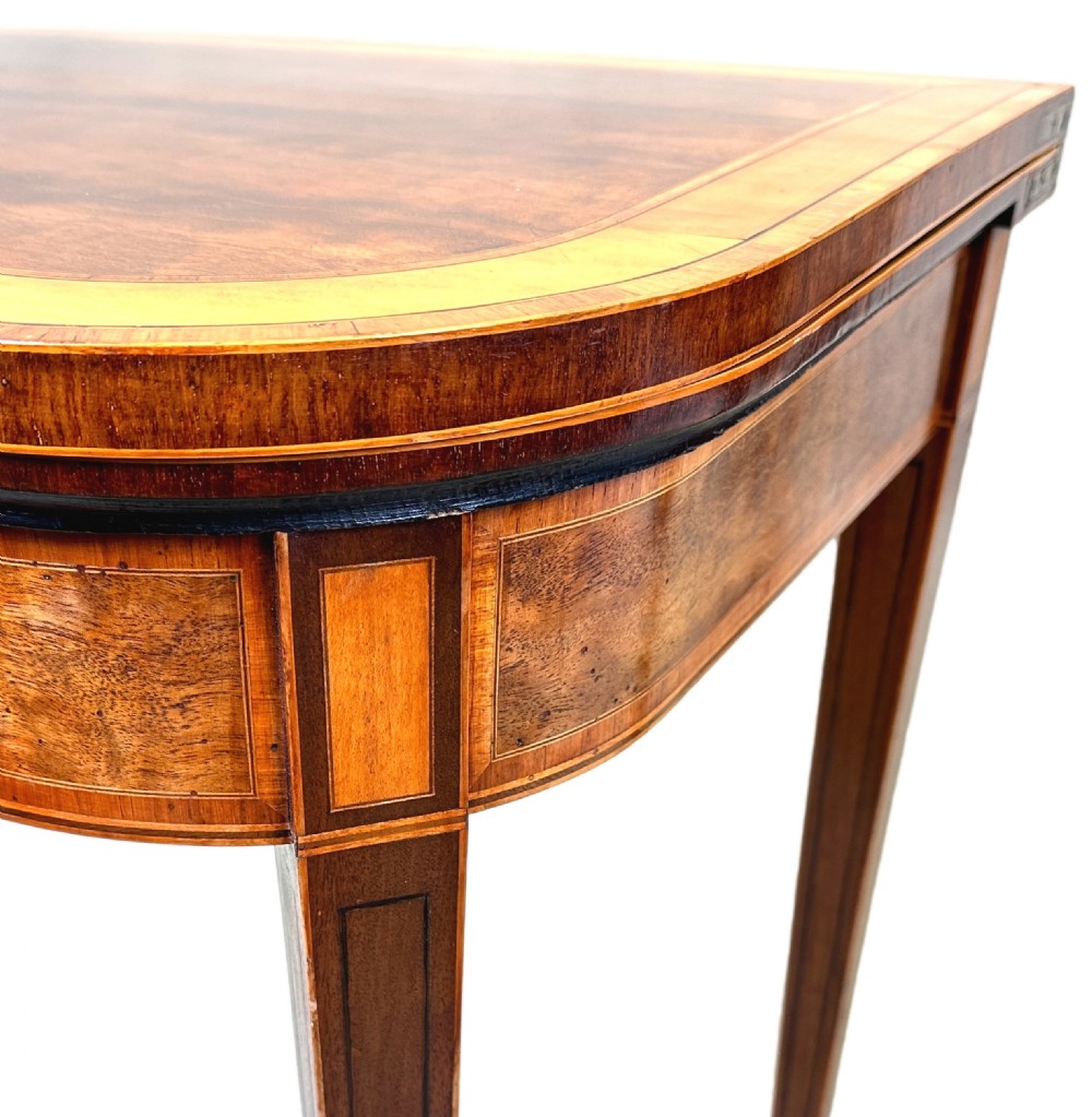 A pair of late Georgian mahogany fold-over card tables featuring satinwood crossbanding and square tapered legs. View X