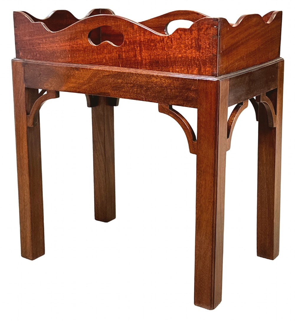 A Georgian mahogany butlers tray featuring a wavy galleried edge with cut-out hand holes, resting atop a matching wooden stand with straight legs and corner brackets.