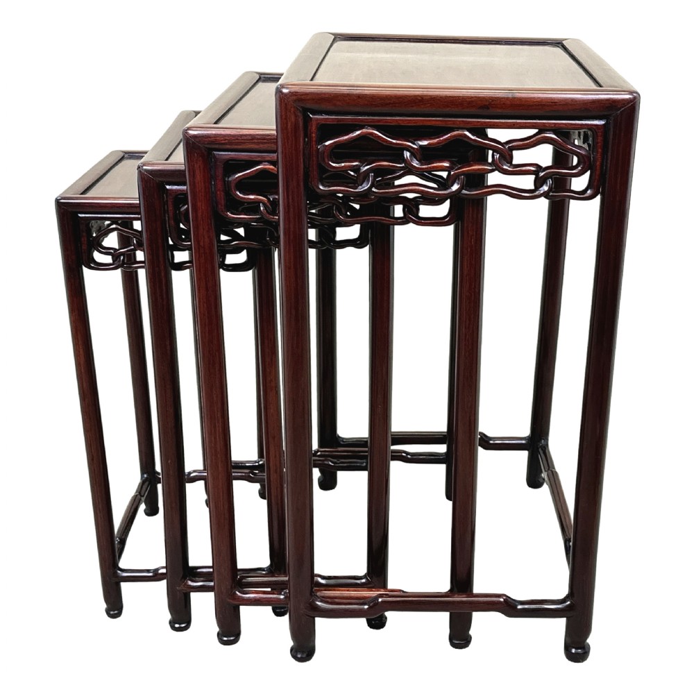 A nest of four graduated dark reddish-brown Oriental hardwood occasional tables featuring pierced carved aprons and slim straight legs. View IV