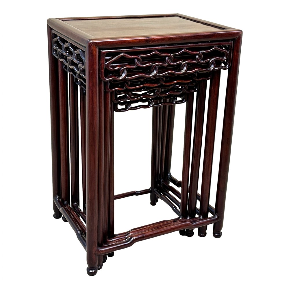 A nest of four graduated dark reddish-brown Oriental hardwood occasional tables featuring pierced carved aprons and slim straight legs. View V