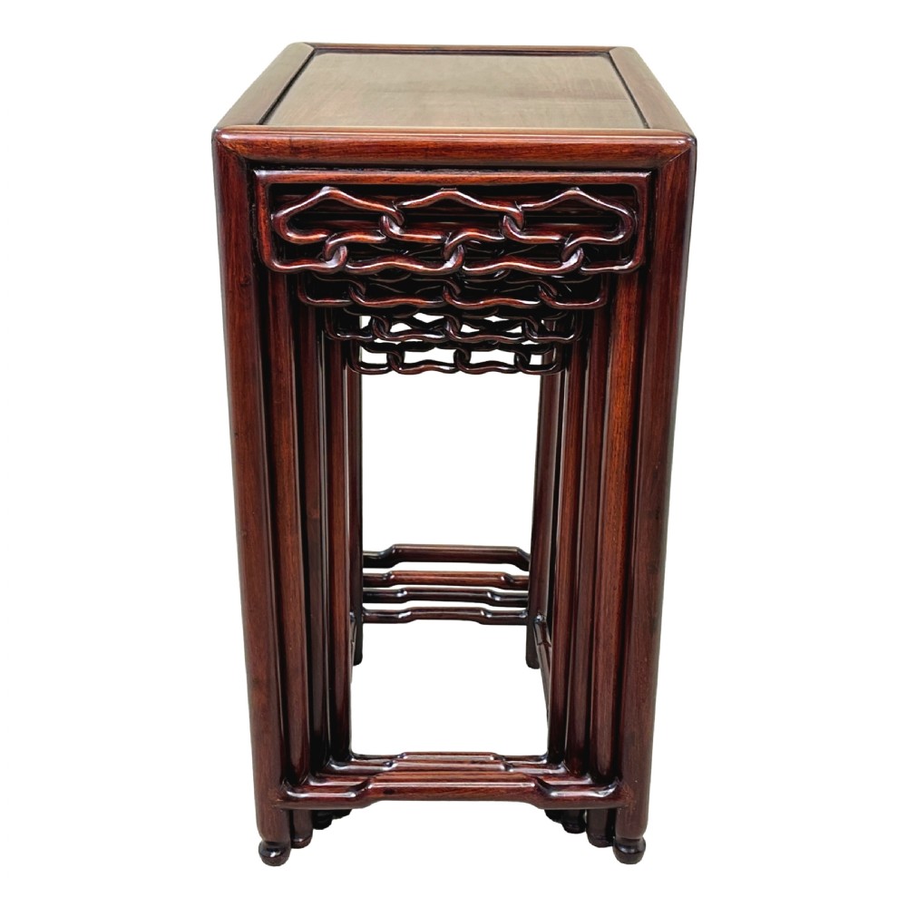 A nest of four graduated dark reddish-brown Oriental hardwood occasional tables featuring pierced carved aprons and slim straight legs. View VII