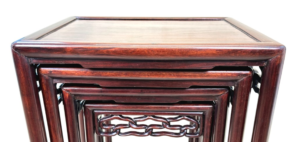 A nest of four graduated dark reddish-brown Oriental hardwood occasional tables featuring pierced carved aprons and slim straight legs. View VIII