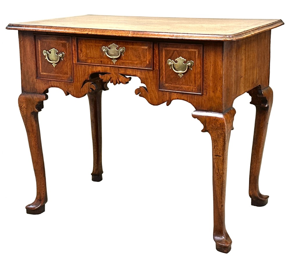 An 18th-century Georgian walnut lowboy table with three drawers, brass drop handles, a carved apron, and cabriole legs.