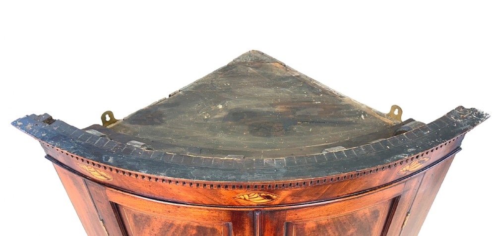 An 18th-century bow-front mahogany corner cupboard featuring double panelled doors, flame veneer, brass keyhole escutcheons, and inlaid shell motifs along the top frieze. View VI