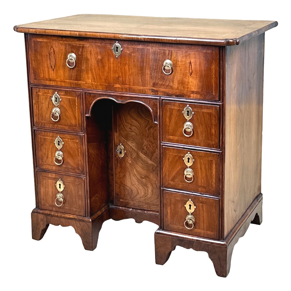 An 18th-century walnut kneehole desk featuring a long upper drawer, six small pedestal drawers, a central recessed cupboard, and brass drop handles on bracket feet.