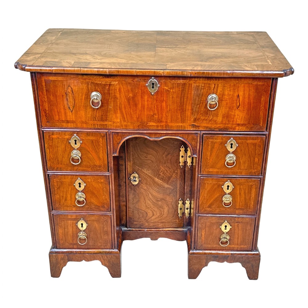An 18th-century walnut kneehole desk featuring a long upper drawer, six small pedestal drawers, a central recessed cupboard, and brass drop handles on bracket feet. View XIV
