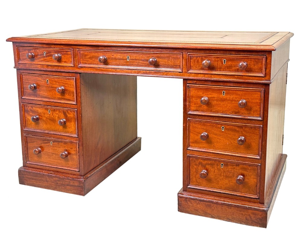 An antique Regency mahogany pedestal desk featuring a gold-tooled leather writing inset and multiple drawers with turned wooden handles on plinth bases.