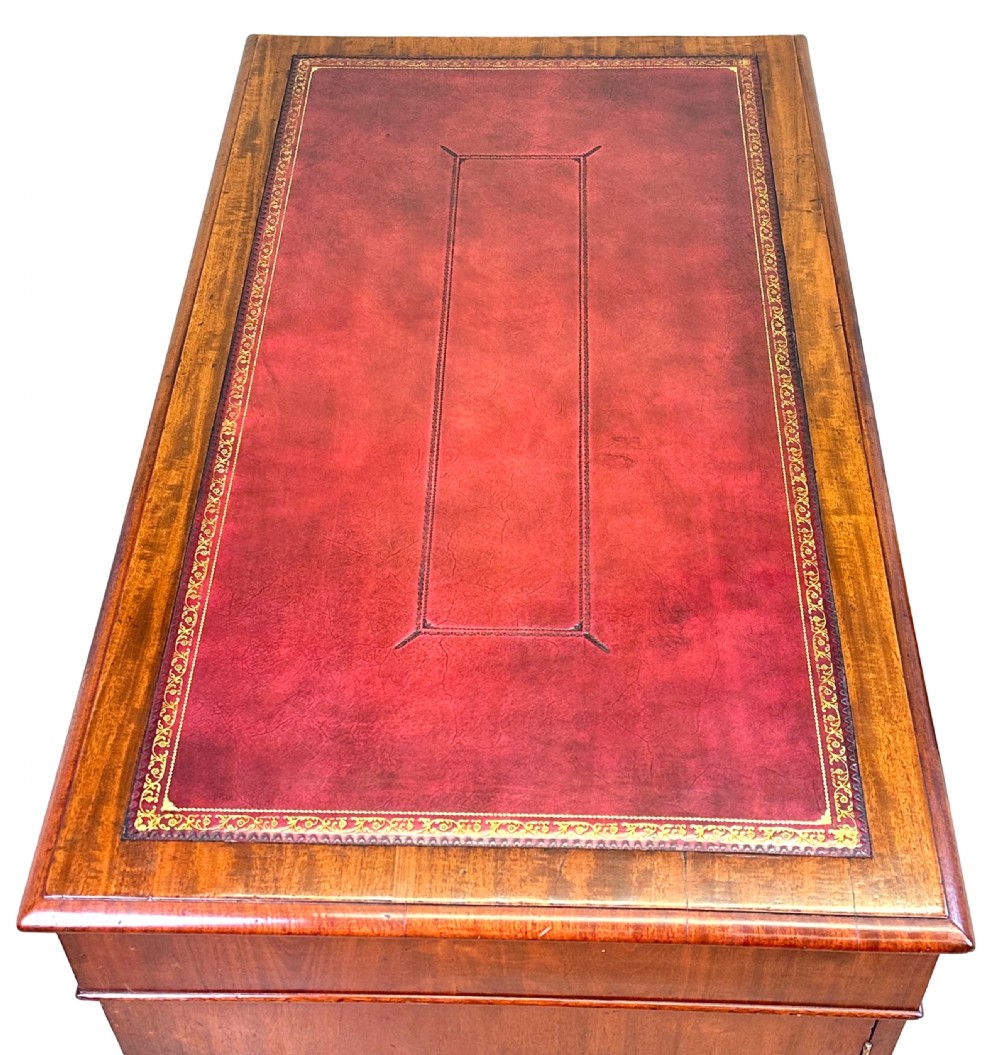 An antique Regency mahogany pedestal desk featuring a gold-tooled leather writing inset and multiple drawers with turned wooden handles on plinth bases. View II