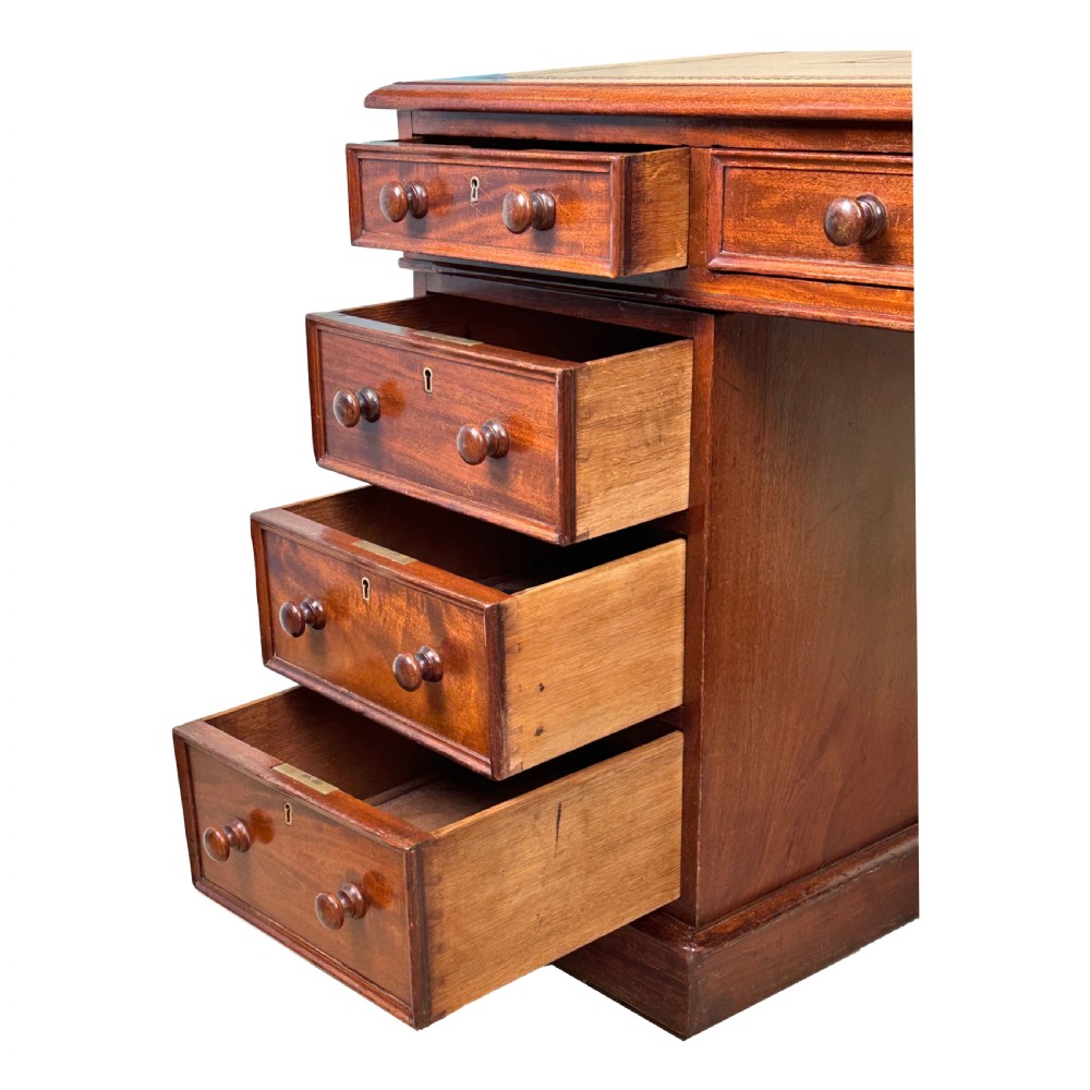 An antique Regency mahogany pedestal desk featuring a gold-tooled leather writing inset and multiple drawers with turned wooden handles on plinth bases. View V