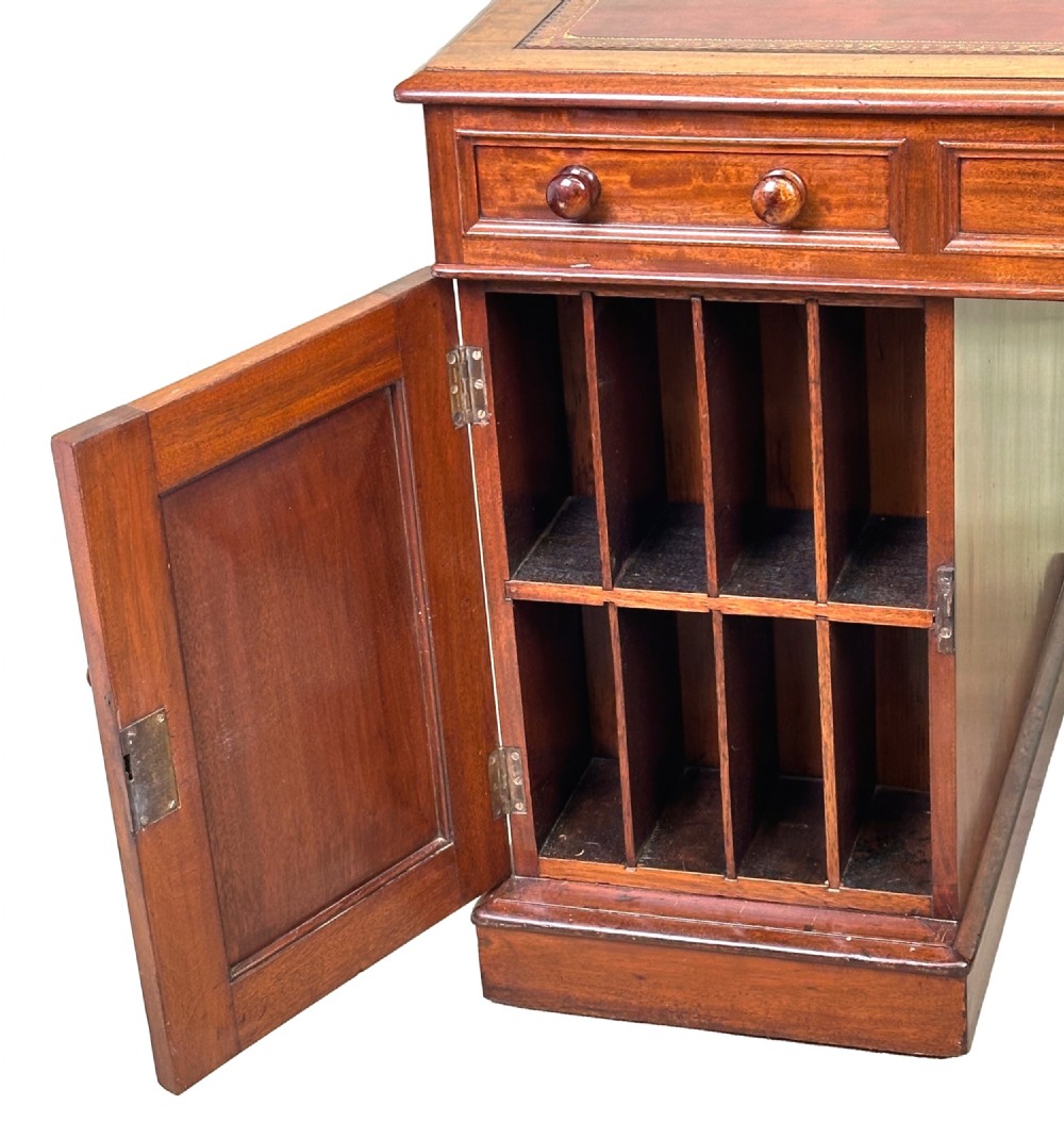 An antique Regency mahogany pedestal desk featuring a gold-tooled leather writing inset and multiple drawers with turned wooden handles on plinth bases. View VI
