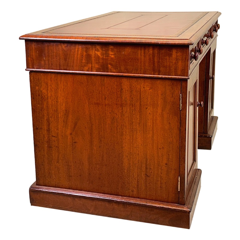 An antique Regency mahogany pedestal desk featuring a gold-tooled leather writing inset and multiple drawers with turned wooden handles on plinth bases. View X