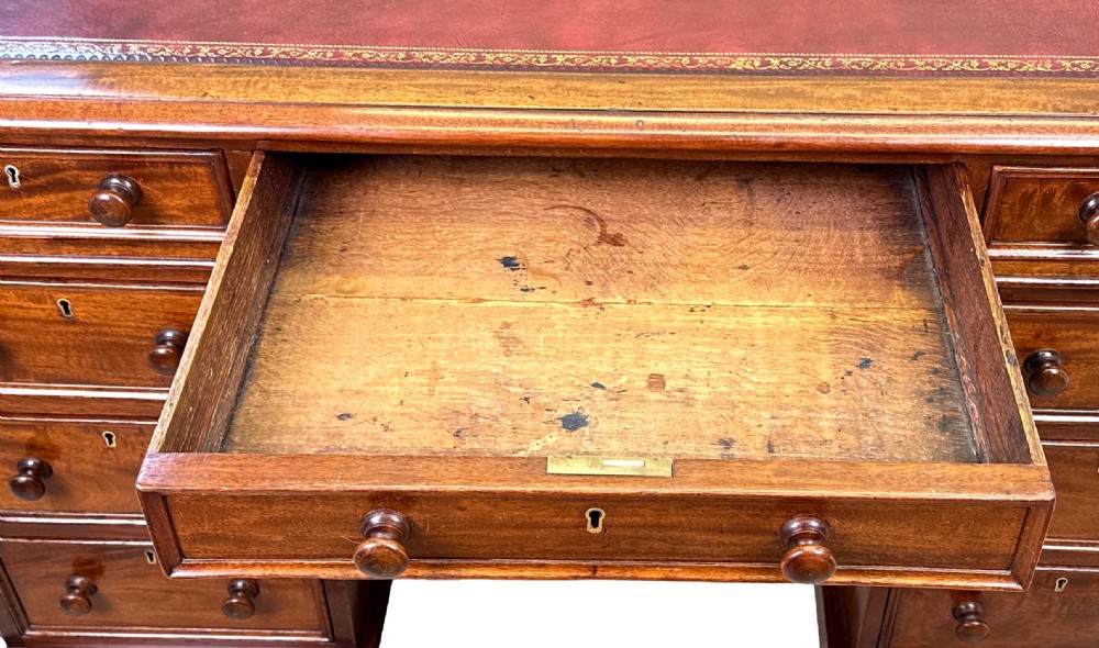 An antique Regency mahogany pedestal desk featuring a gold-tooled leather writing inset and multiple drawers with turned wooden handles on plinth bases. View XIII