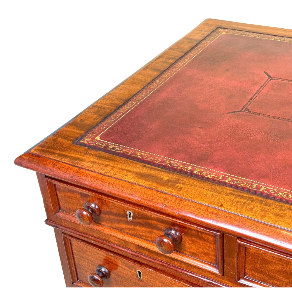 An antique Regency mahogany pedestal desk featuring a gold-tooled leather writing inset and multiple drawers with turned wooden handles on plinth bases. View XV