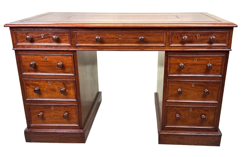 An antique Regency mahogany pedestal desk featuring a gold-tooled leather writing inset and multiple drawers with turned wooden handles on plinth bases. View XVI