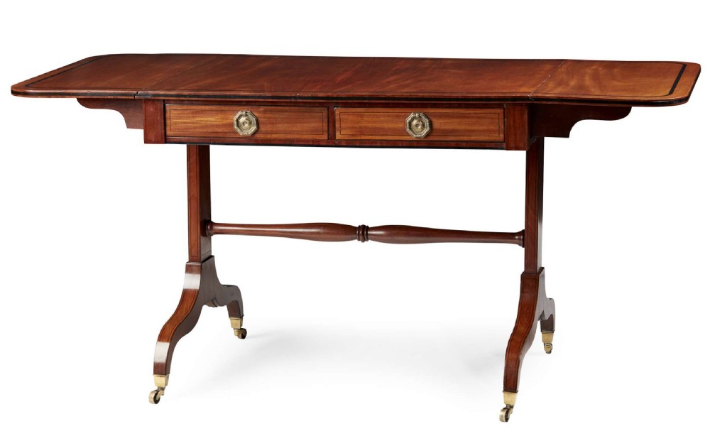 A 19th-century Regency mahogany sofa table featuring two drop leaves, two frieze drawers with octagonal brass handles, a turned stretcher, and splay legs on brass castors.