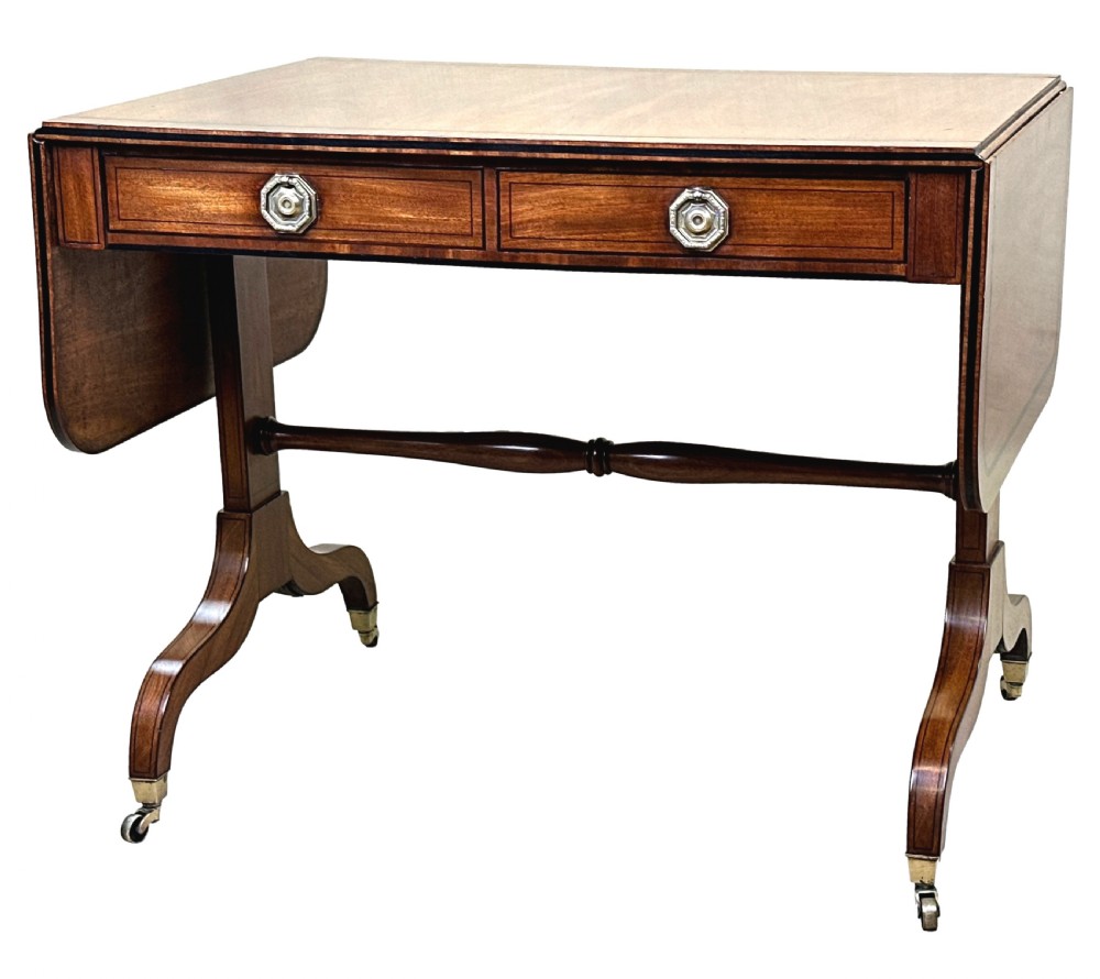 A 19th-century Regency mahogany sofa table featuring two drop leaves, two frieze drawers with octagonal brass handles, a turned stretcher, and splay legs on brass castors. View III