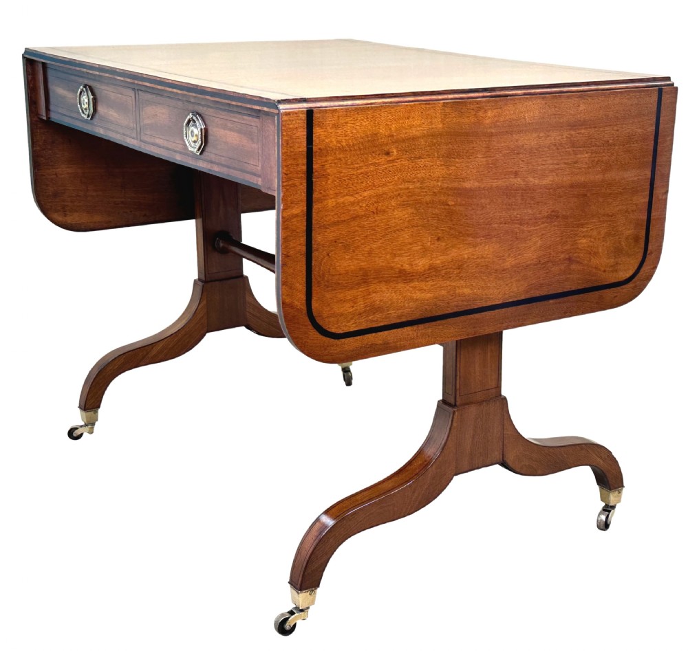 A 19th-century Regency mahogany sofa table featuring two drop leaves, two frieze drawers with octagonal brass handles, a turned stretcher, and splay legs on brass castors. View VI