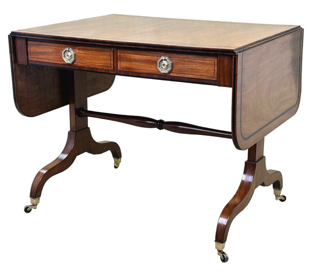 A 19th-century Regency mahogany sofa table featuring two drop leaves, two frieze drawers with octagonal brass handles, a turned stretcher, and splay legs on brass castors. View VIII