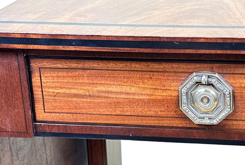 A 19th-century Regency mahogany sofa table featuring two drop leaves, two frieze drawers with octagonal brass handles, a turned stretcher, and splay legs on brass castors. View IX