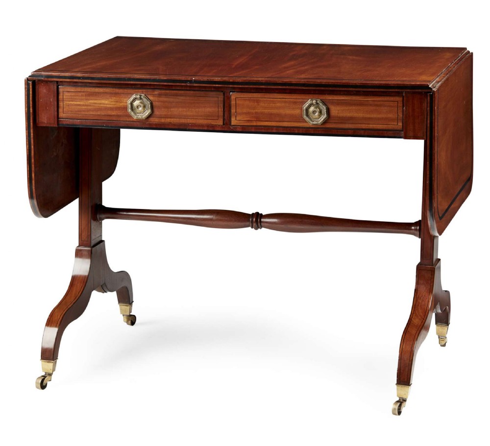 A 19th-century Regency mahogany sofa table featuring two drop leaves, two frieze drawers with octagonal brass handles, a turned stretcher, and splay legs on brass castors. View X