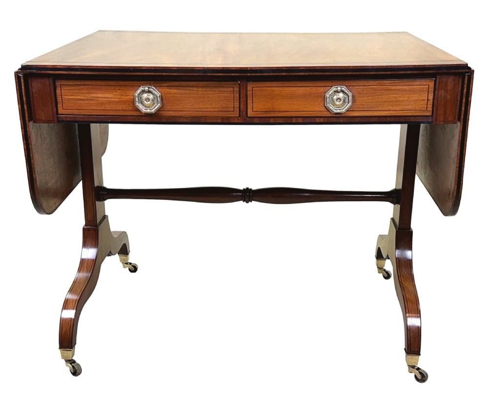 A 19th-century Regency mahogany sofa table featuring two drop leaves, two frieze drawers with octagonal brass handles, a turned stretcher, and splay legs on brass castors. View XI