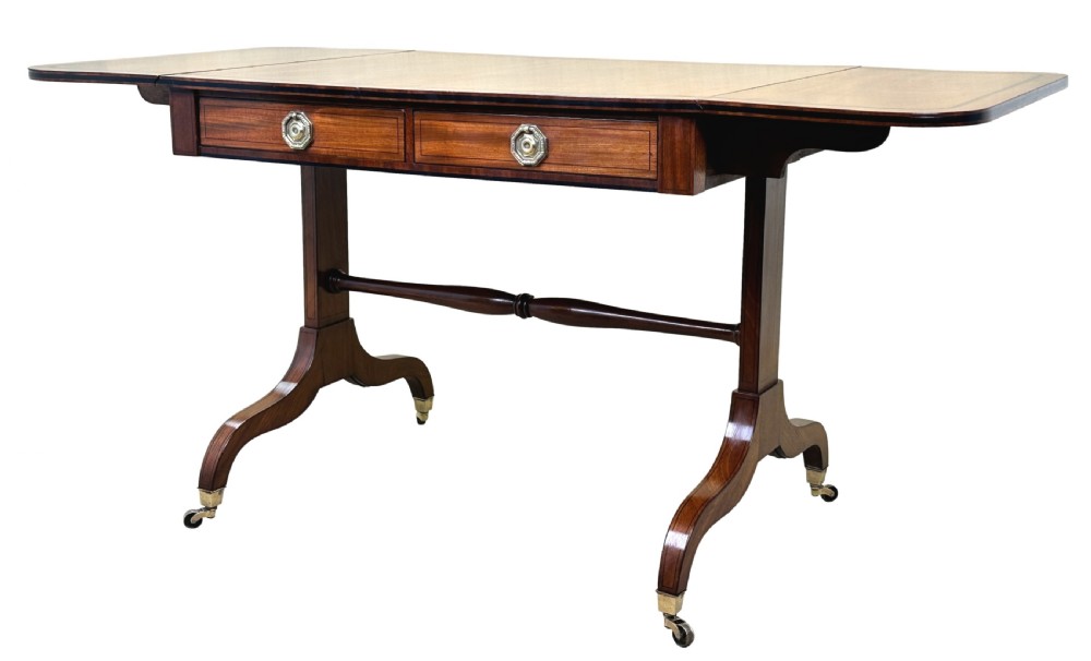 A 19th-century Regency mahogany sofa table featuring two drop leaves, two frieze drawers with octagonal brass handles, a turned stretcher, and splay legs on brass castors. View XII