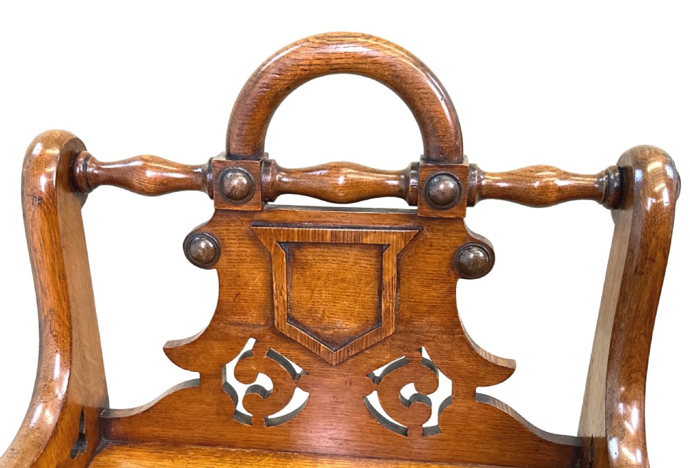 A matched pair of 19th-century carved oak hall seats featuring arched top handle rails, shield-carved back panels, pierced side aprons, and turned cross stretchers. View II