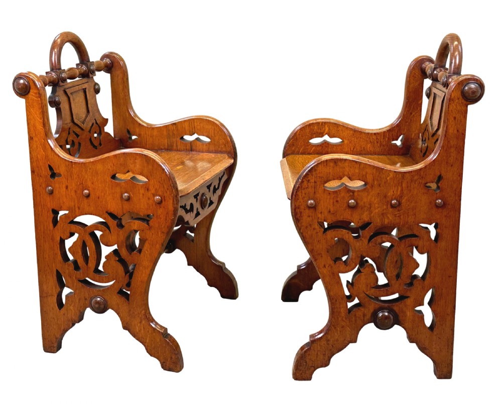 A matched pair of 19th-century carved oak hall seats featuring arched top handle rails, shield-carved back panels, pierced side aprons, and turned cross stretchers. View III