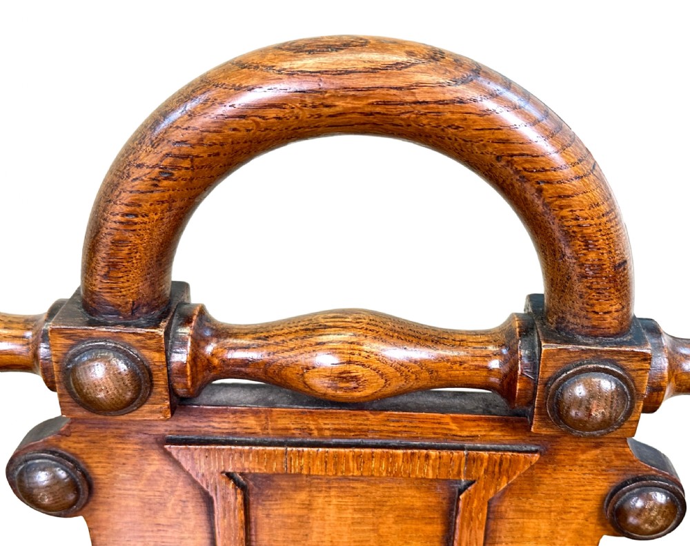 A matched pair of 19th-century carved oak hall seats featuring arched top handle rails, shield-carved back panels, pierced side aprons, and turned cross stretchers. View V