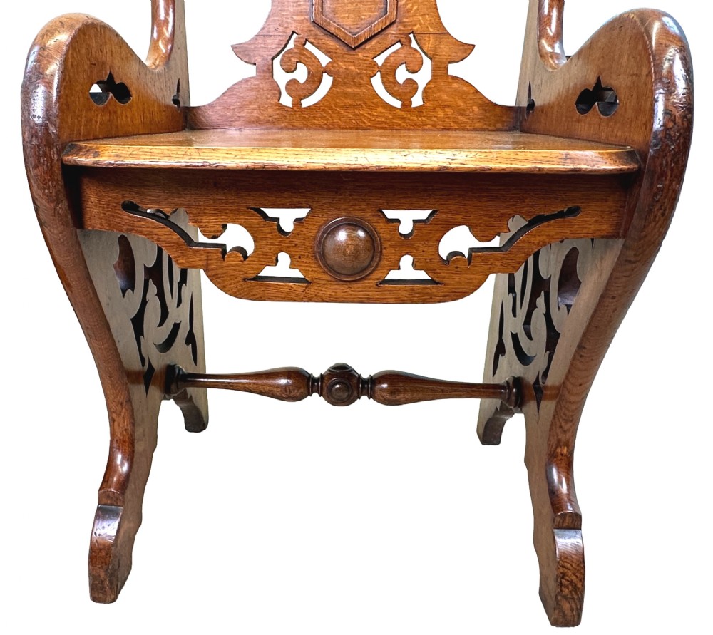 A matched pair of 19th-century carved oak hall seats featuring arched top handle rails, shield-carved back panels, pierced side aprons, and turned cross stretchers. View VII