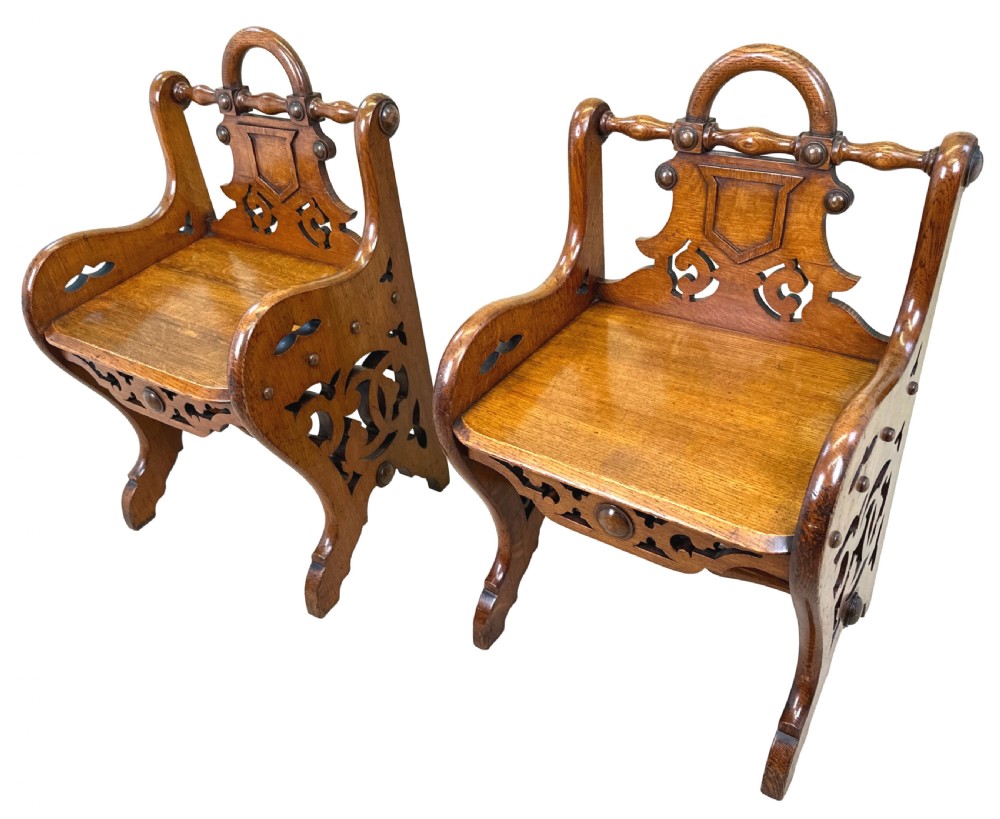 A matched pair of 19th-century carved oak hall seats featuring arched top handle rails, shield-carved back panels, pierced side aprons, and turned cross stretchers. View IX