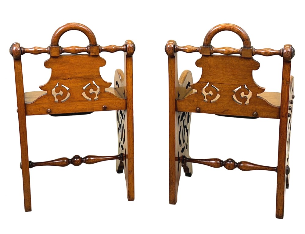 A matched pair of 19th-century carved oak hall seats featuring arched top handle rails, shield-carved back panels, pierced side aprons, and turned cross stretchers. View X