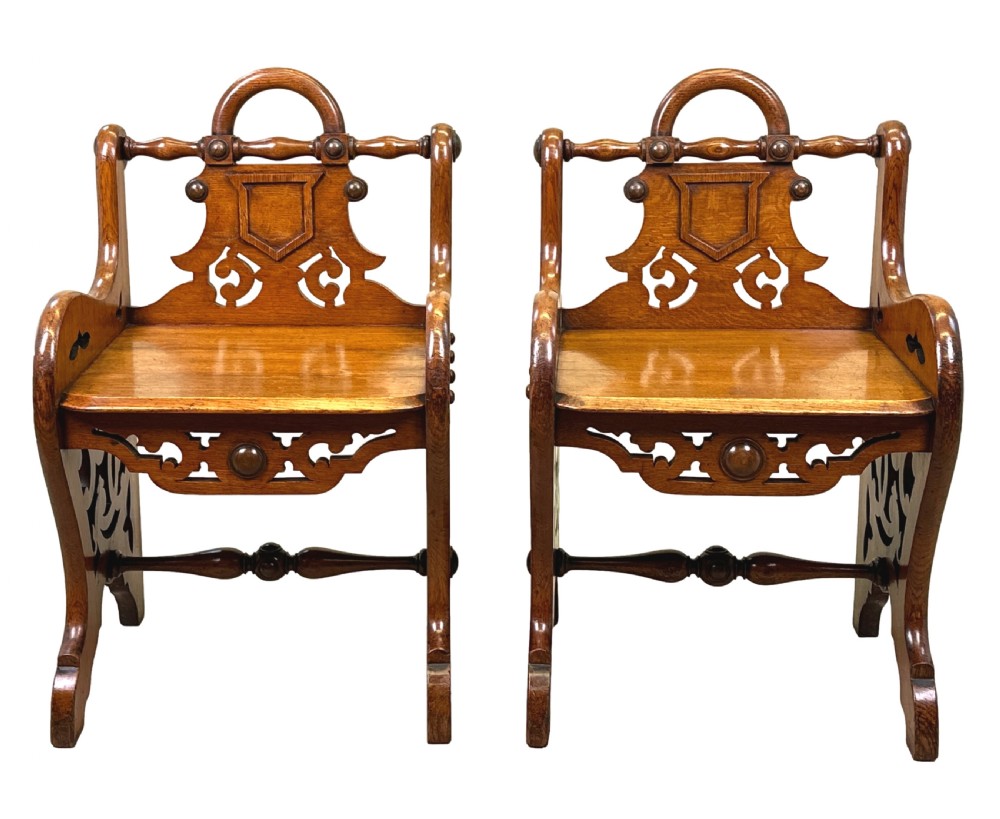 A matched pair of 19th-century carved oak hall seats featuring arched top handle rails, shield-carved back panels, pierced side aprons, and turned cross stretchers. View XIV