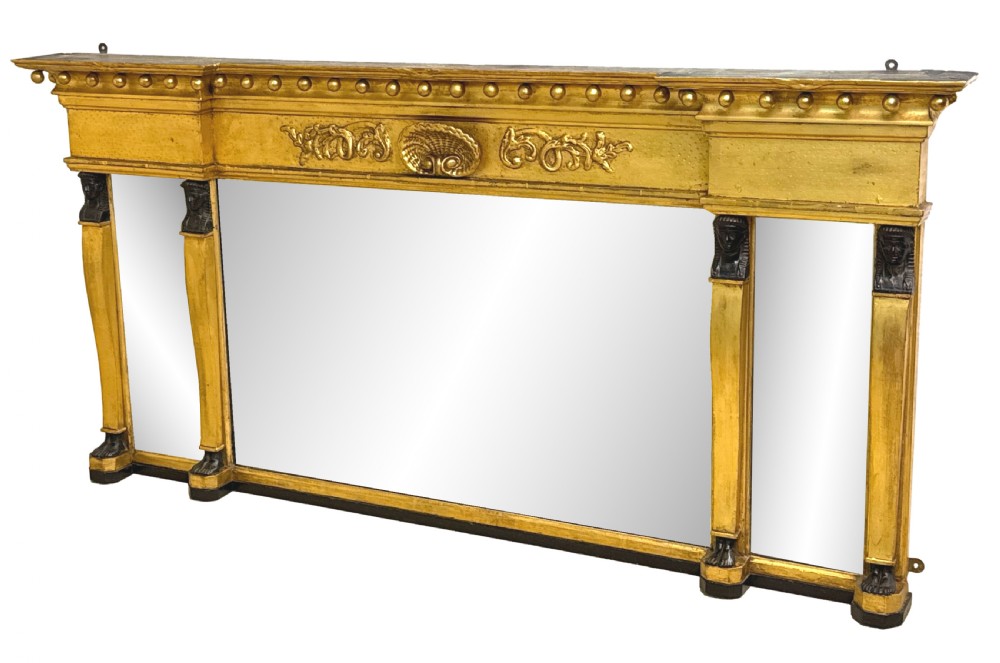 A wide Regency giltwood overmantel mirror featuring three mirror plates, ball moulding along the top cornice, central carved shell frieze, and black Egyptian head pilasters.