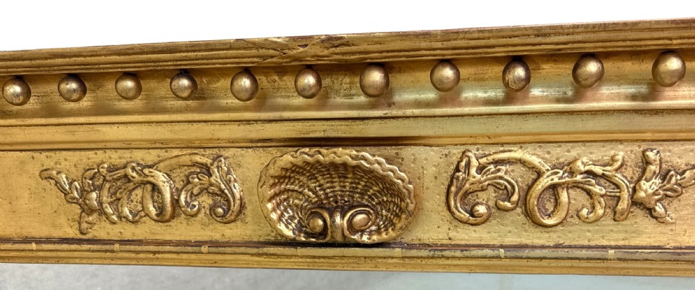 A wide Regency giltwood overmantel mirror featuring three mirror plates, ball moulding along the top cornice, central carved shell frieze, and black Egyptian head pilasters. View IV