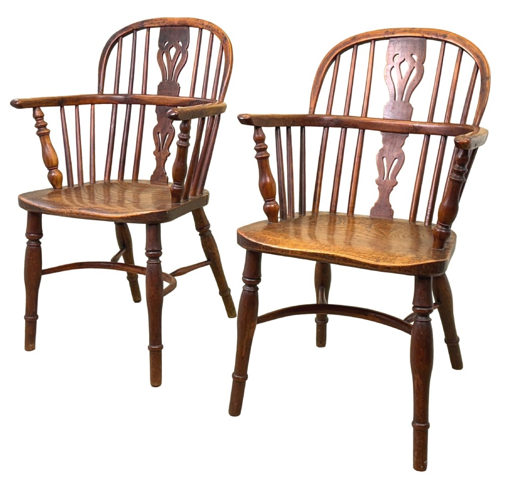 A pair of 19th-century yew wood Windsor armchairs featuring steam-bent hoop backs, pierced central back splats, turned spindle supports, and contoured saddle seats.