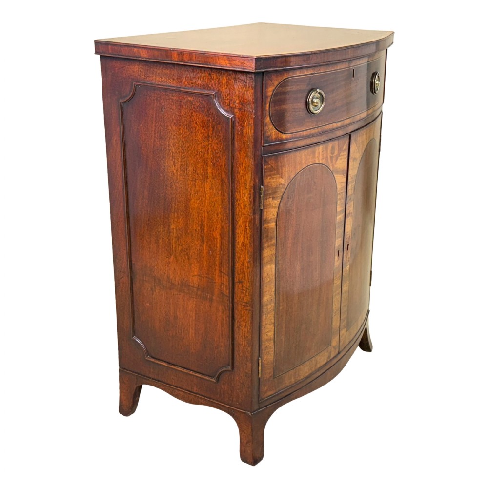 An 18th-century Georgian mahogany bowfront side cupboard featuring two arched inlaid doors, a top frieze drawer with brass handles, and splay feet. View VI