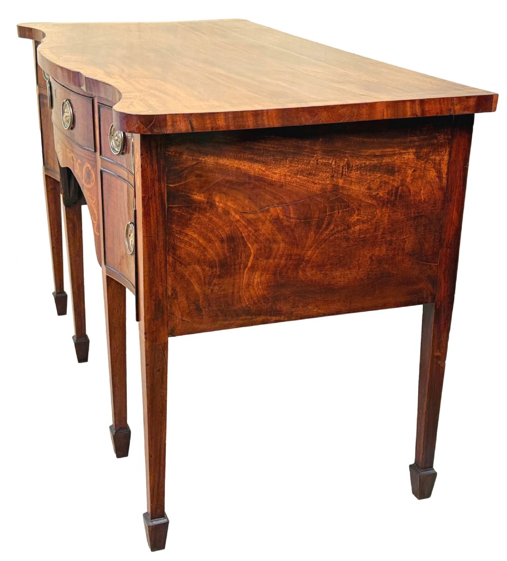 A small Georgian mahogany sideboard featuring a serpentine front, floral marquetry inlay, multiple drawers with brass ring handles, and tapered square legs with spade feet. View IV